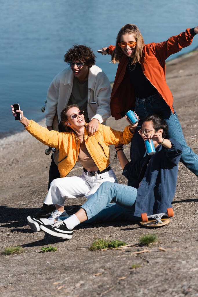 mulher feliz com smartphone e refrigerante pode se divertir com amigos inter-raciais no dique - Foto, Imagem