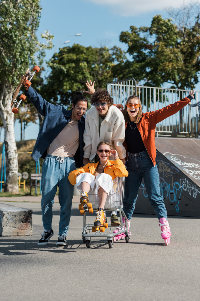 взволнованные мультиэтнические фигуристы движутся корзину с счастливой женщиной в скейт-парке - Фото, изображение