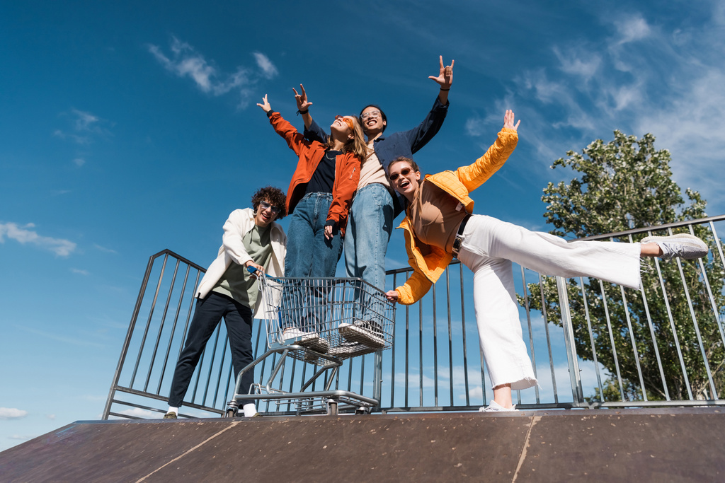 vue à faible angle de joyeux amis interraciaux s'amuser avec panier sur la rampe dans le skate park - Photo, image