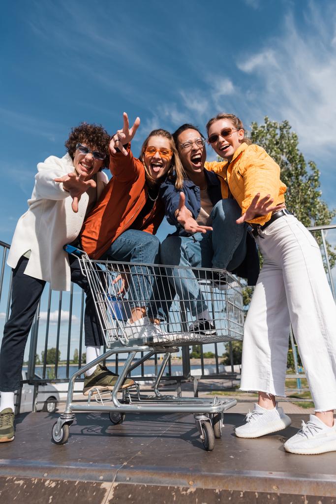 interracial přátelé v nákupním košíku gestikulace a křik na skate rampě - Fotografie, Obrázek