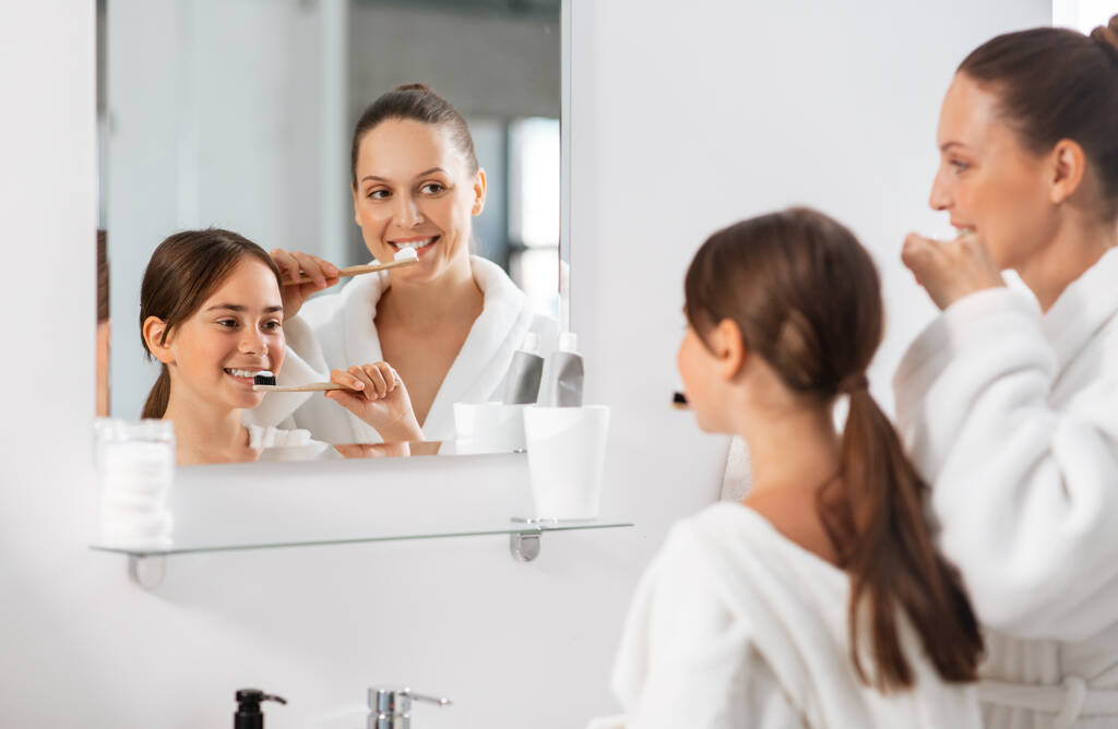 beauté, hygiène, concept matin et personnes - mère et fille souriantes heureuses avec brosses à dents brossant les dents à la salle de bain - Photo, image