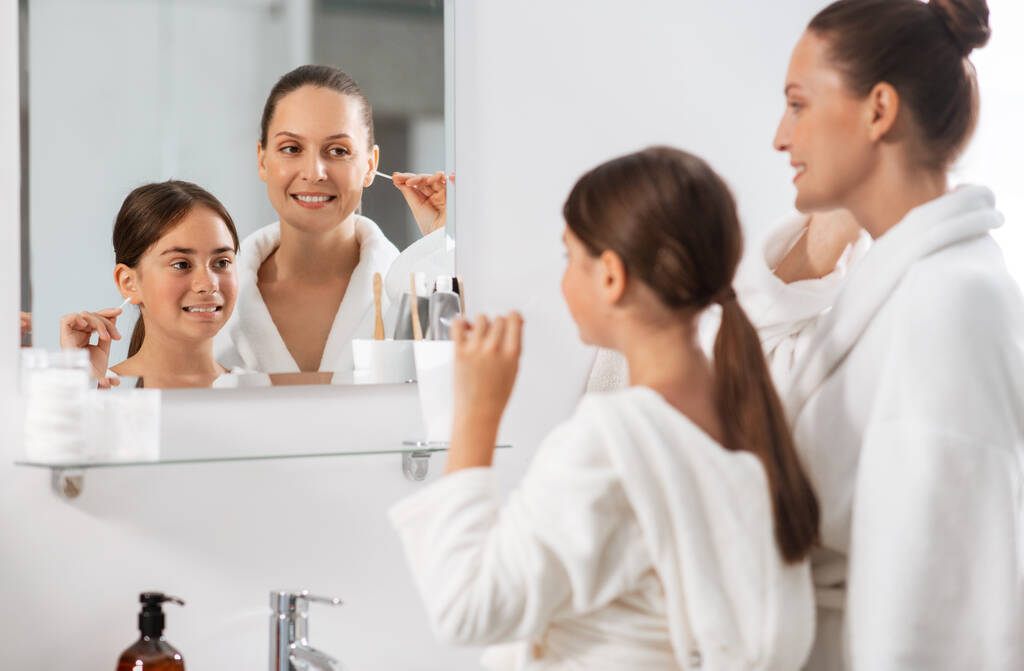 kauneus, hygienia, aamu ja ihmiset konsepti onnellinen hymyilevä äiti ja tytär puhdistaa korvat puuvillapyyhkeillä ja etsivät peiliä kylpyhuoneessa - Valokuva, kuva