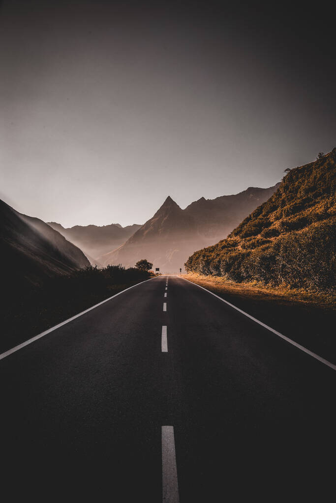 Kırsal bir alanda arka planda kayalık dağlar olan asfalt bir yolun dikey görüntüsü. - Fotoğraf, Görsel