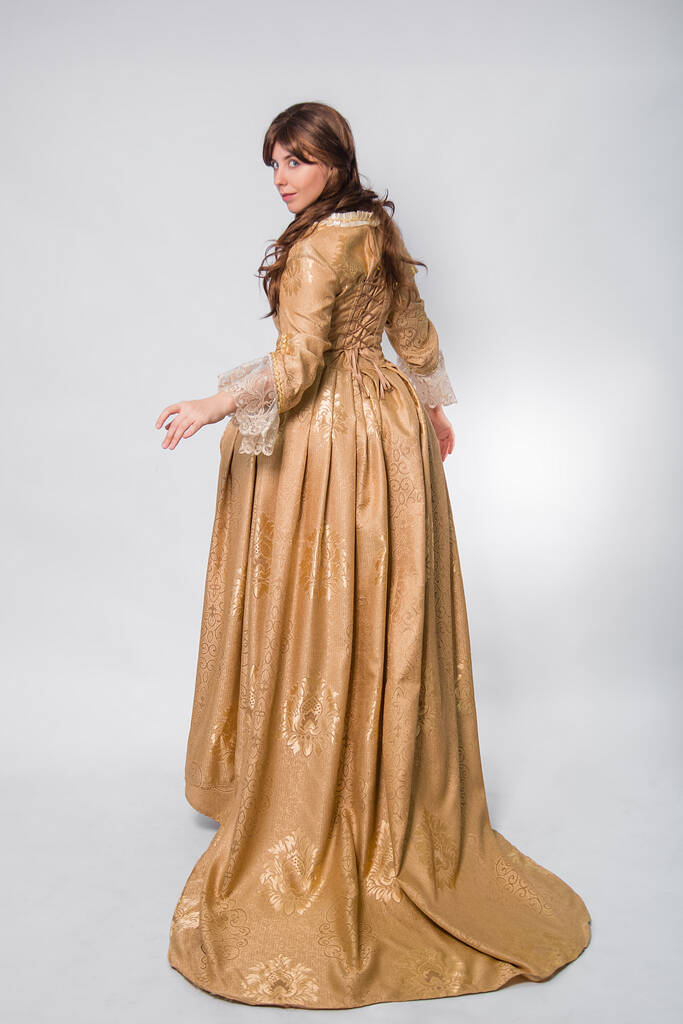 Portrait pleine longueur d'une femme en robe d'or dans le style de l'ère rococo, debout avec son dos vers l'avant et posant isolé sur un fond blanc. - Photo, image