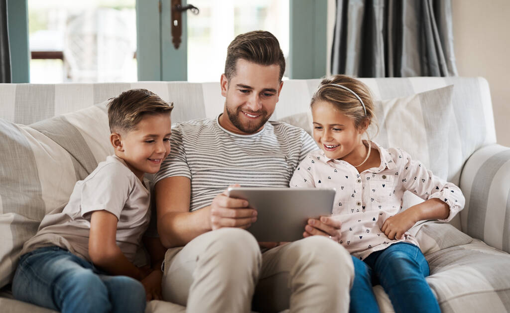 Snímek roztomilé holčičky a chlapce pomocí digitálního tabletu s jejich otcem na pohovce doma. - Fotografie, Obrázek