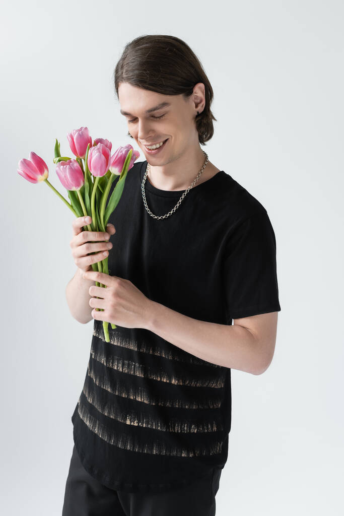 Feliz hombre elegante con tulipanes aislados en gris  - Foto, imagen
