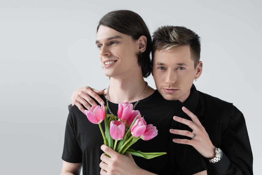 Young gay embracing boyfriend with tulip flowers isolated on grey  - Photo, Image