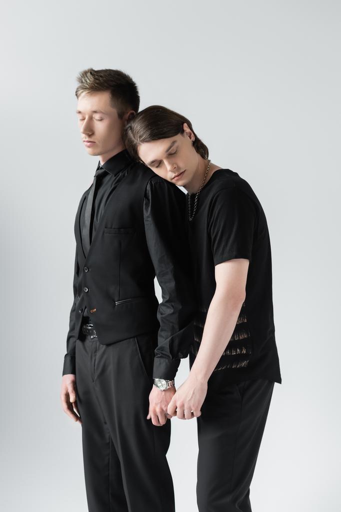 młody gej para z zamknięty oczy trzymając ręce izolowane na szary  - Zdjęcie, obraz
