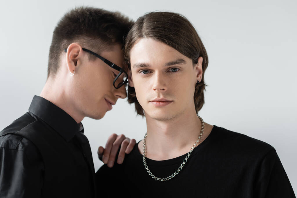 Bruneta gayové při pohledu na kameru poblíž přítele v brýlích izolovaných na šedé  - Fotografie, Obrázek