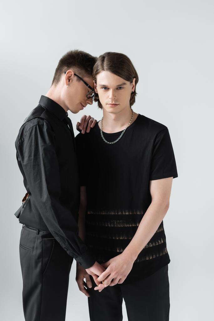 Молода пара гей в чорному одязі тримає руки ізольовані на сірому
  - Фото, зображення