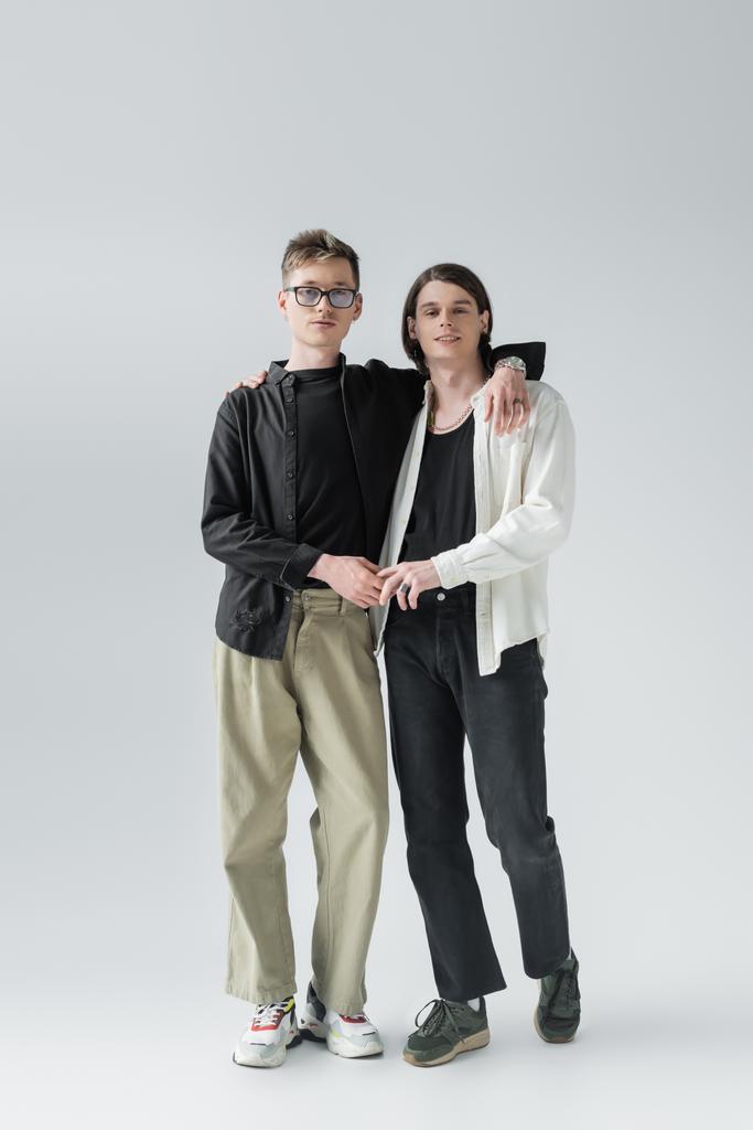 Volle Länge der Homosexuell Paar hält Hände und Umarmung auf grauem Hintergrund  - Foto, Bild
