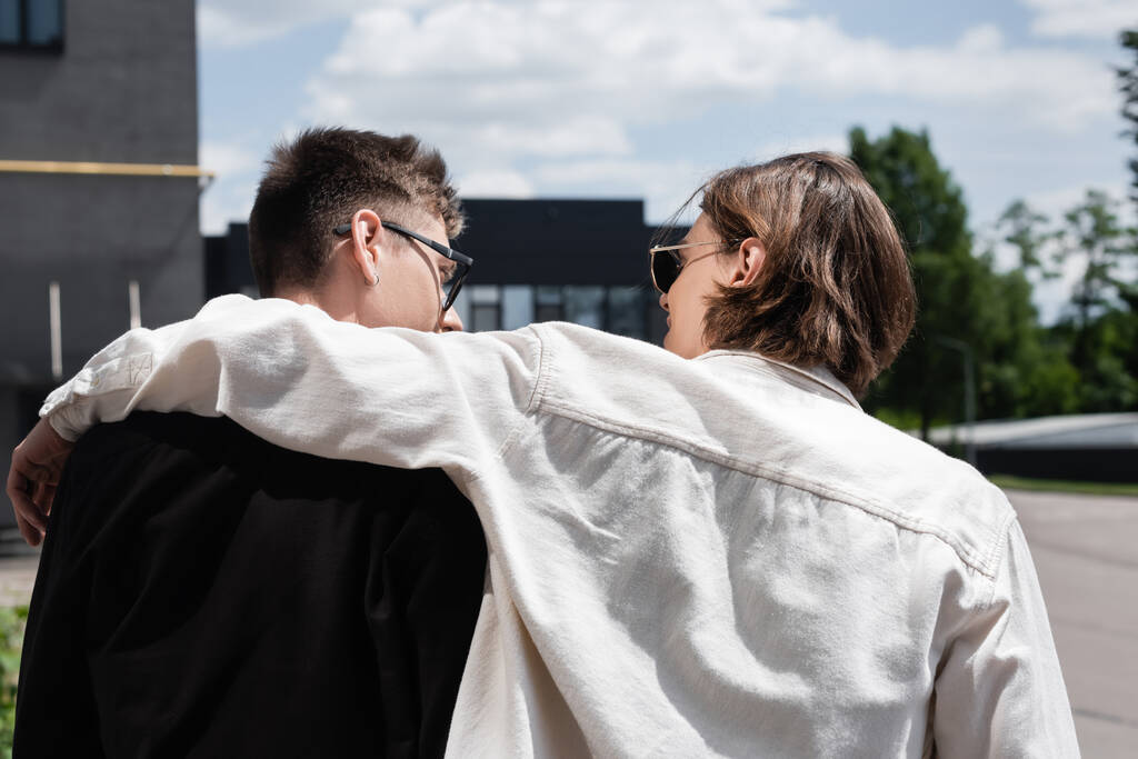 Vista laterale dell'uomo in occhiali da sole che abbraccia il fidanzato sulla strada urbana  - Foto, immagini