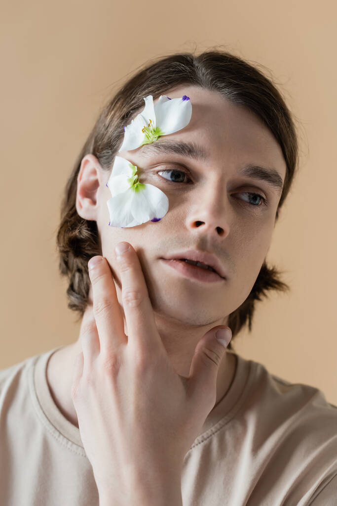 Yüzünde çiçek olan genç bir adam Bej rengi gözlerden uzak bir şekilde bakıyor  - Fotoğraf, Görsel