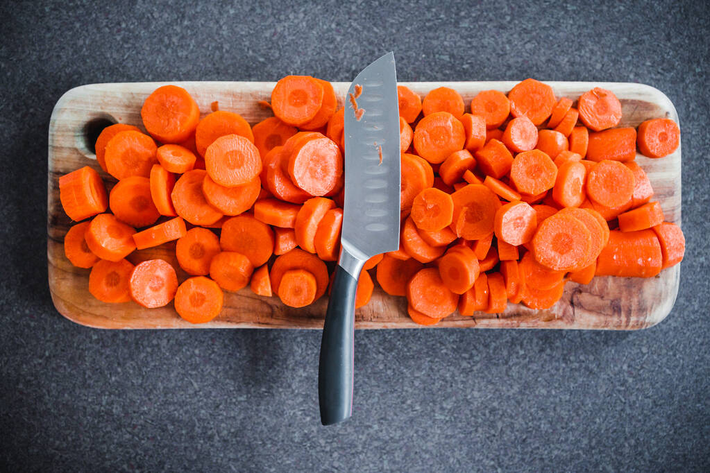close-up of fresh carrots getting sliced on wooden chopping board with knife in the centre, concept of simple natural healthy ingredients - Photo, Image