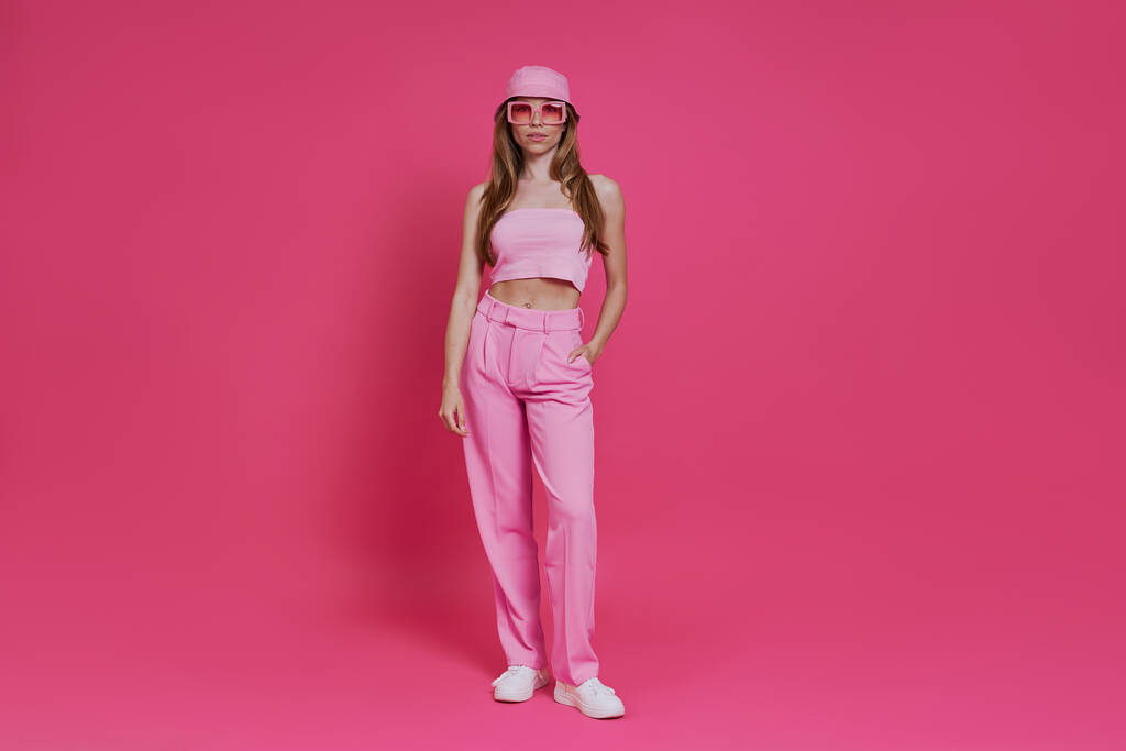Longitud completa de la hermosa mujer joven en ropa de moda de pie sobre fondo rosa - Foto, imagen