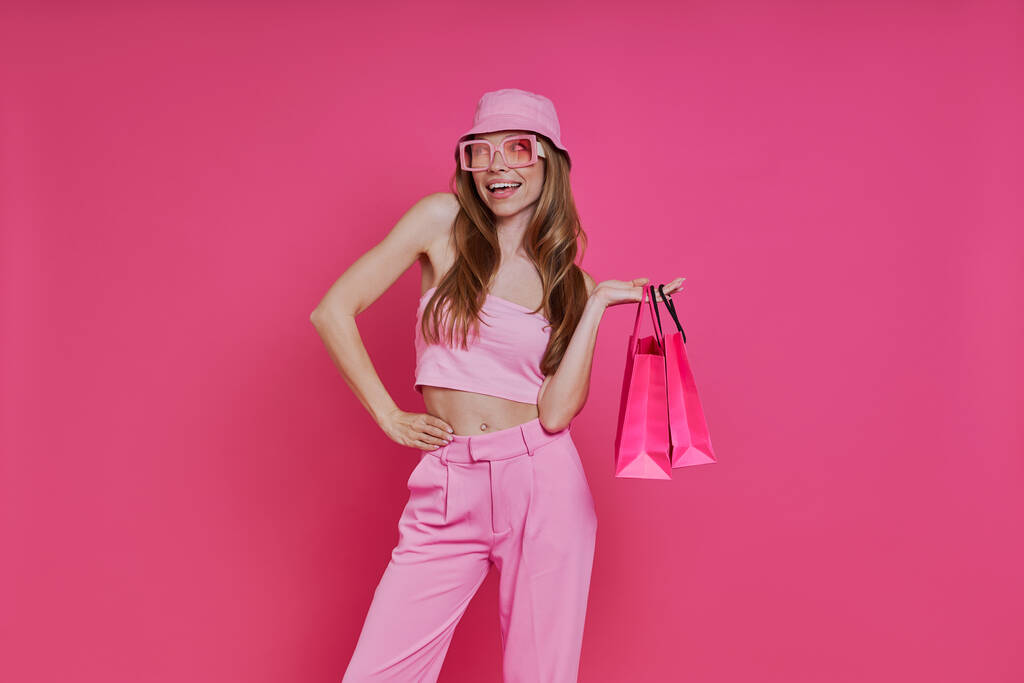 Nachdenkliche junge Frau mit Einkaufstaschen vor rosa Hintergrund - Foto, Bild