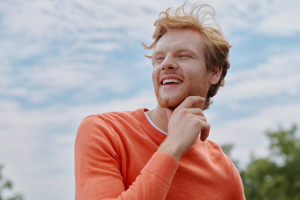 Rento nuori punapää mies kädestä leualla ja hymyilee seistessään ulkona - Valokuva, kuva