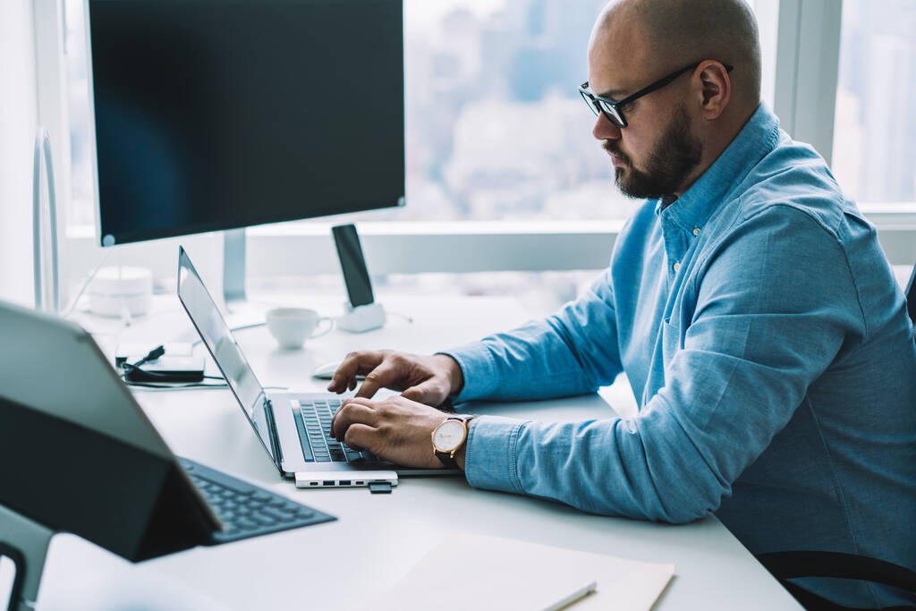 サイドビュー作物男性オフィスワーカーで正式なシャツで机の上に座っている現代的なガジェットと光の職場でノートパソコンのキーボードを入力 - 写真・画像