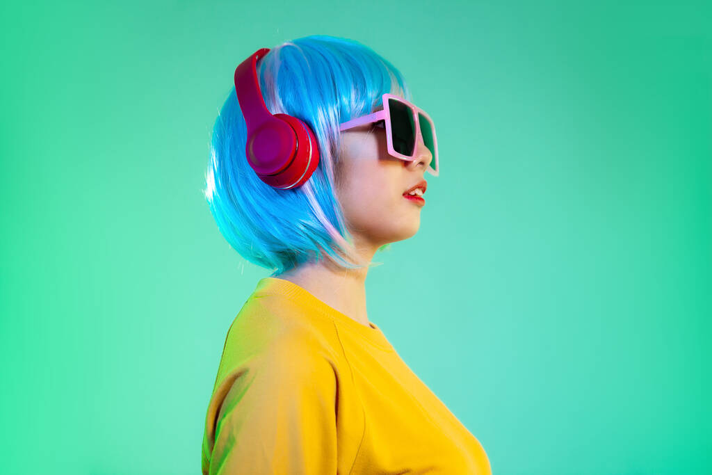 νεαρές Ασιάτισσες με ακουστικά απομονωμένες σε πράσινο φόντο νέον. Ανθρώπινα συναισθήματα. - Φωτογραφία, εικόνα