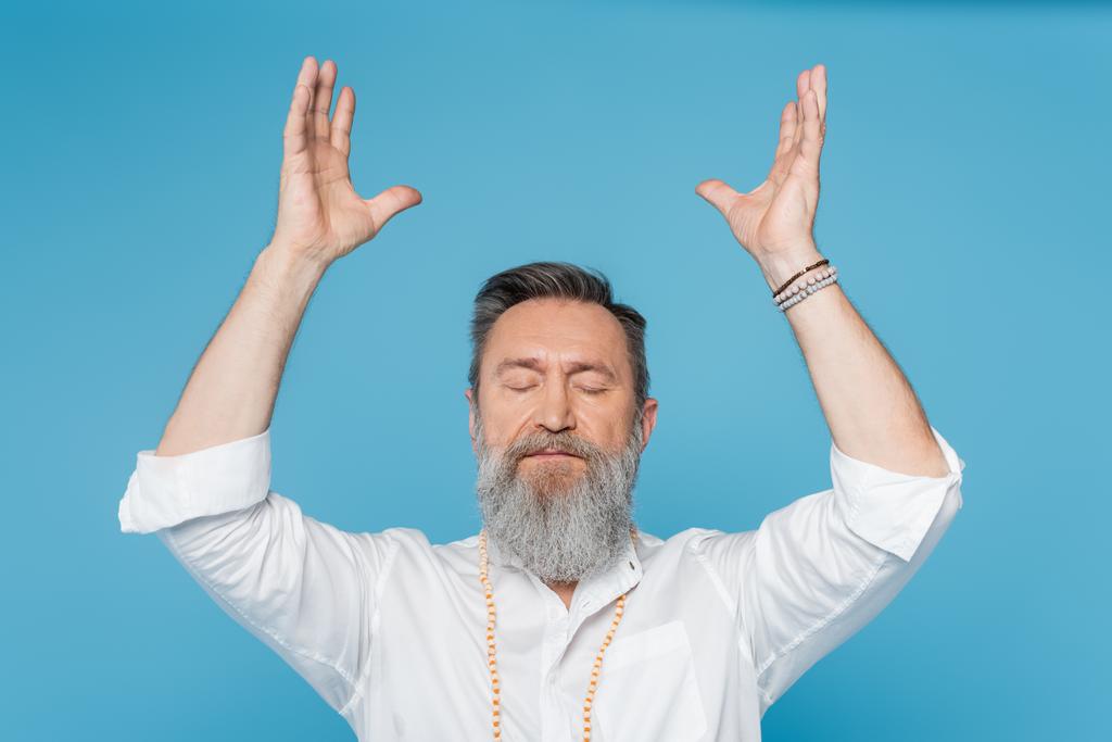bearded guru man meditating with closed eyes and raised hands isolated on blue - Photo, Image