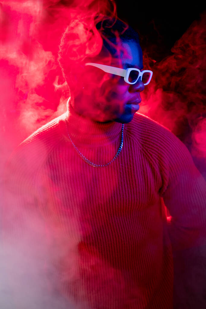 Neonový hipster. Moderní móda. Noční klub. Sebevědomý atraktivní muž portrét v kouři proudí jasné červené světlo na tmavém pozadí studia. - Fotografie, Obrázek
