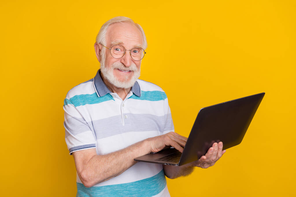 Porträt von attraktiven fröhlichen grauhaarigen Mann mit Laptop Film anschauen isoliert über helle gelbe Farbe Hintergrund. - Foto, Bild