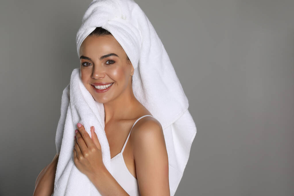 Όμορφη νεαρή γυναίκα με πετσέτες σε γκρι φόντο - Φωτογραφία, εικόνα