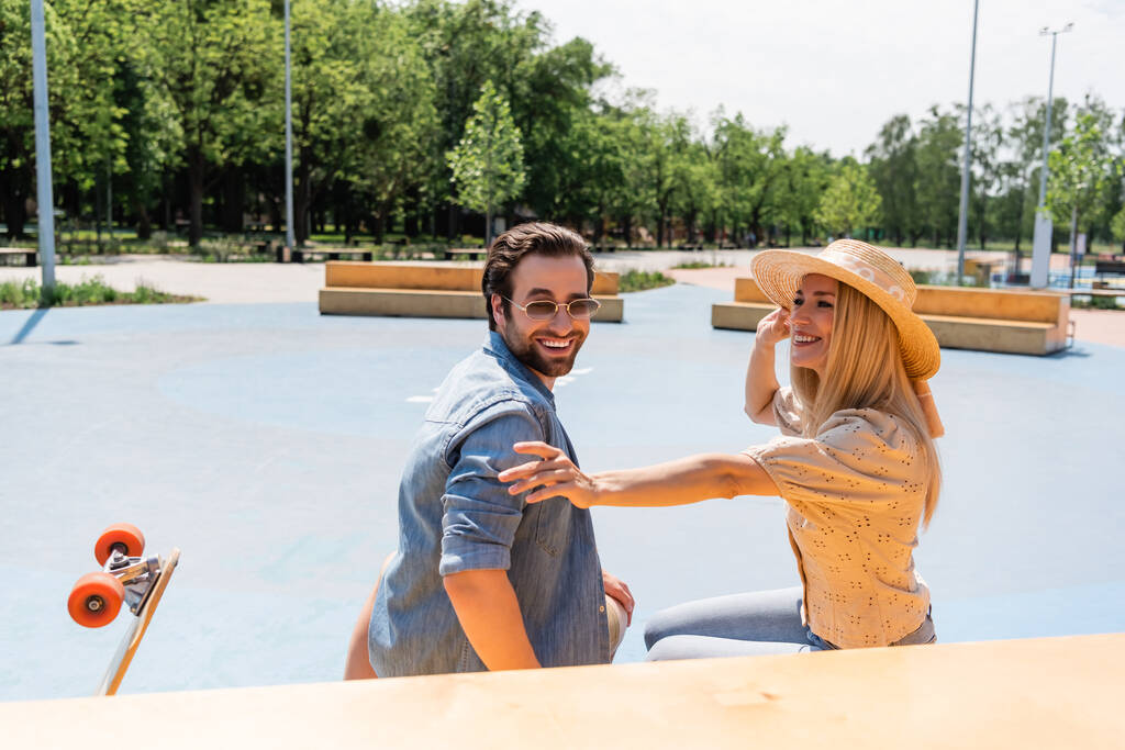 Usmívající se pár tráví čas v blízkosti longboard v skate parku  - Fotografie, Obrázek