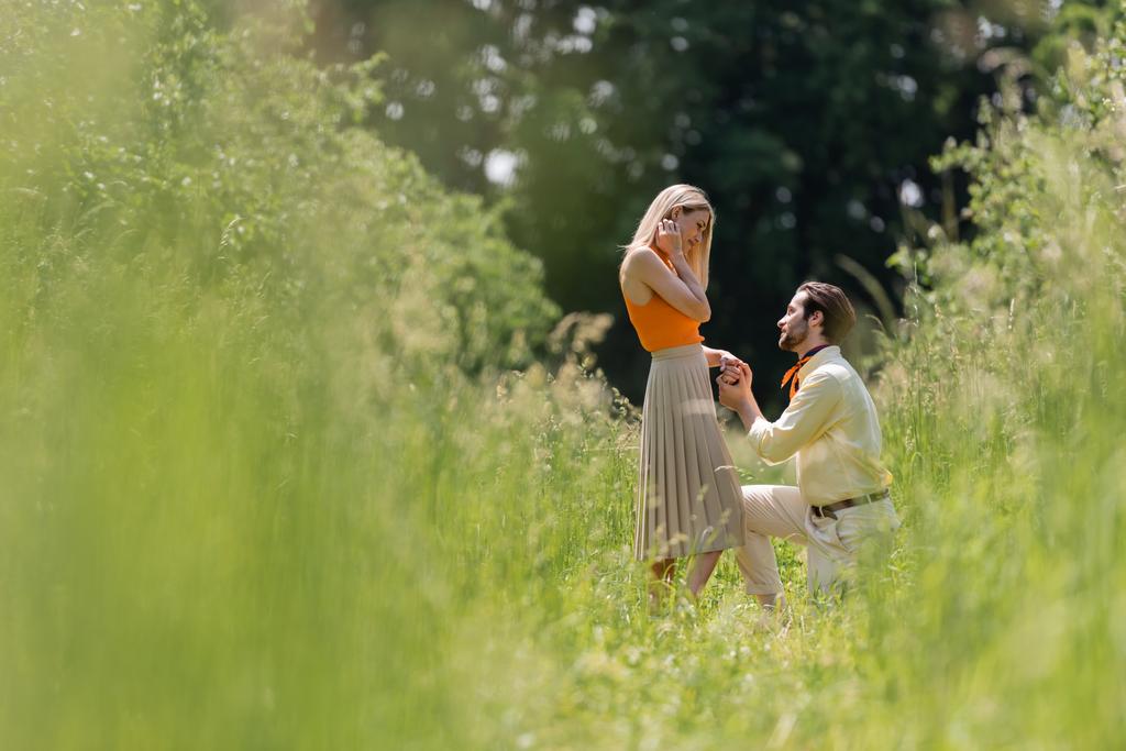Zijaanzicht van stijlvolle man hand vasthouden van vriendin terwijl knielen in de zomer park  - Foto, afbeelding