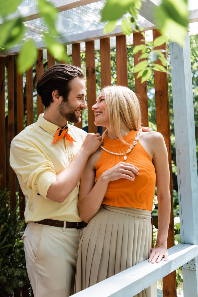 side view of stylish man wearing necklace on stylish girlfriend on terrace of cafe  - Photo, Image