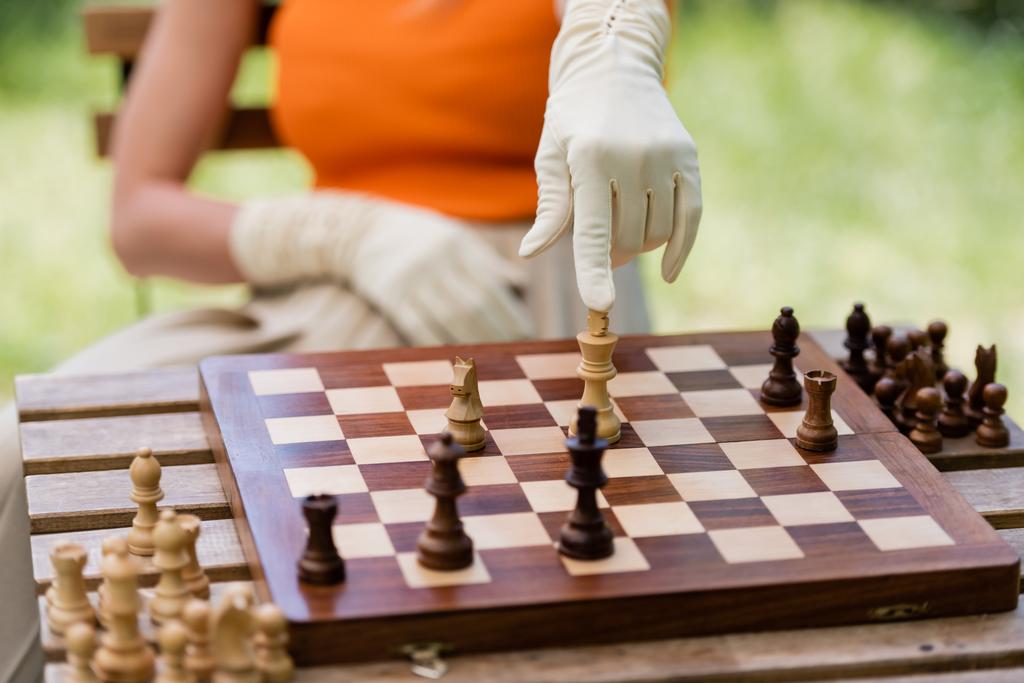 Vista recortada de una mujer elegante apuntando a la figura de ajedrez a bordo en el parque  - Foto, Imagen
