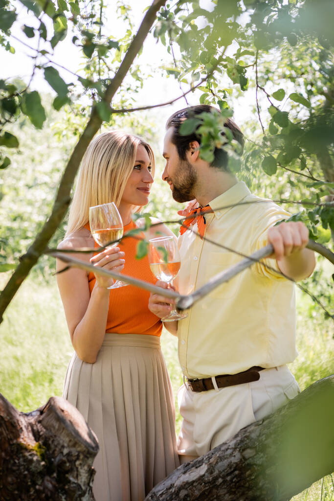 Modna para trzymająca wino i patrząca na siebie w letnim parku  - Zdjęcie, obraz