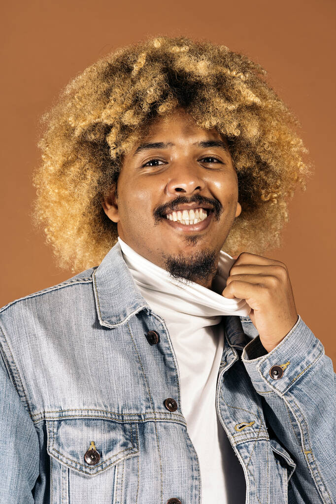 Stockfoto van vrolijke afro man lachend en kijkend naar camera in studio geschoten tegen bruine achtergrond. - Foto, afbeelding