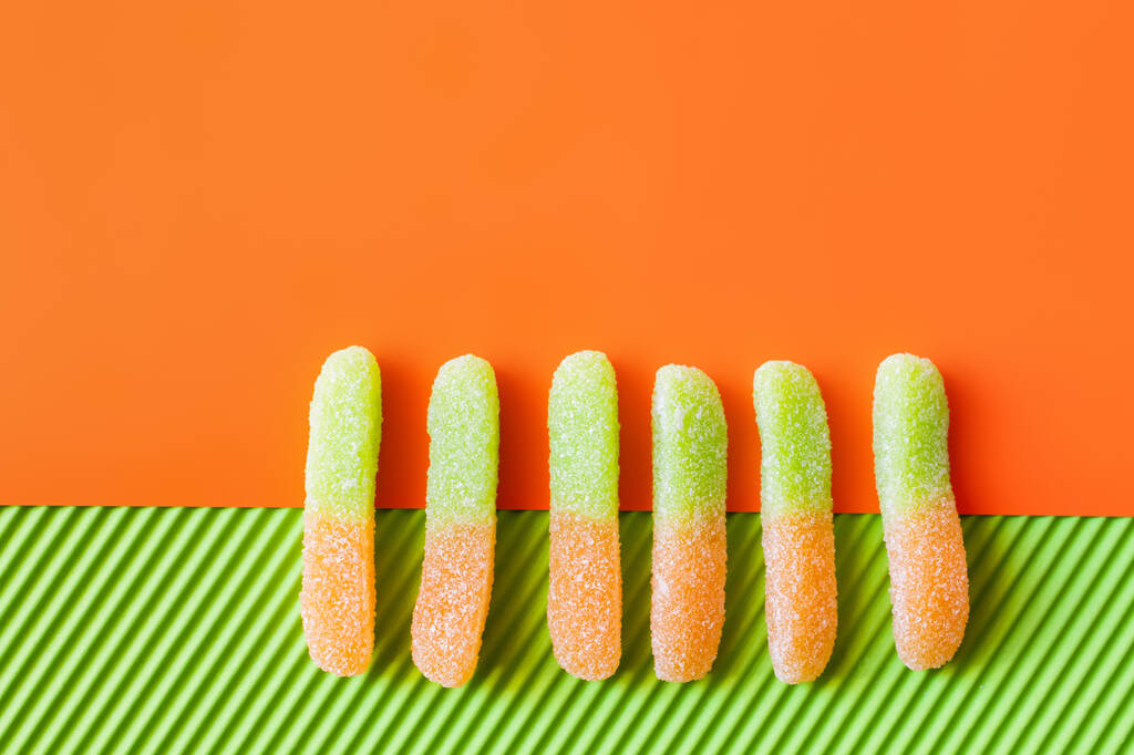 Top view of jelly sweets on orange and green surface  - Photo, Image