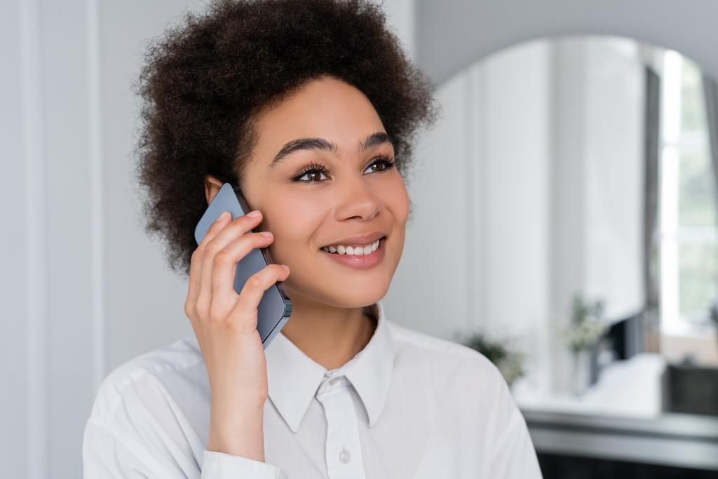 vreugdevolle Afrikaanse Amerikaanse vrouw praten op mobiele telefoon in de moderne woonkamer - Foto, afbeelding