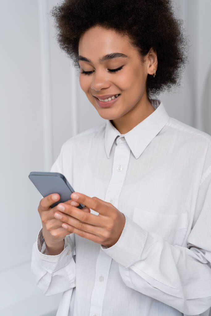 радісна афроамериканська жінка обмінюється повідомленнями на смартфоні вдома
  - Фото, зображення