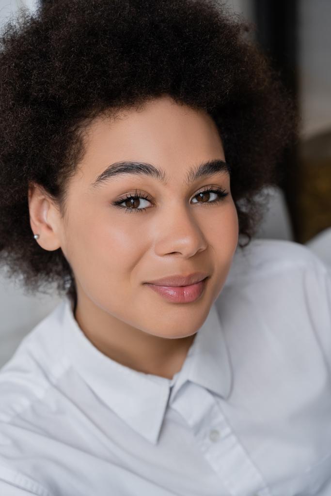 Hochwinkelaufnahme einer lächelnden und lockigen Afroamerikanerin im weißen Hemd mit Kragen  - Foto, Bild