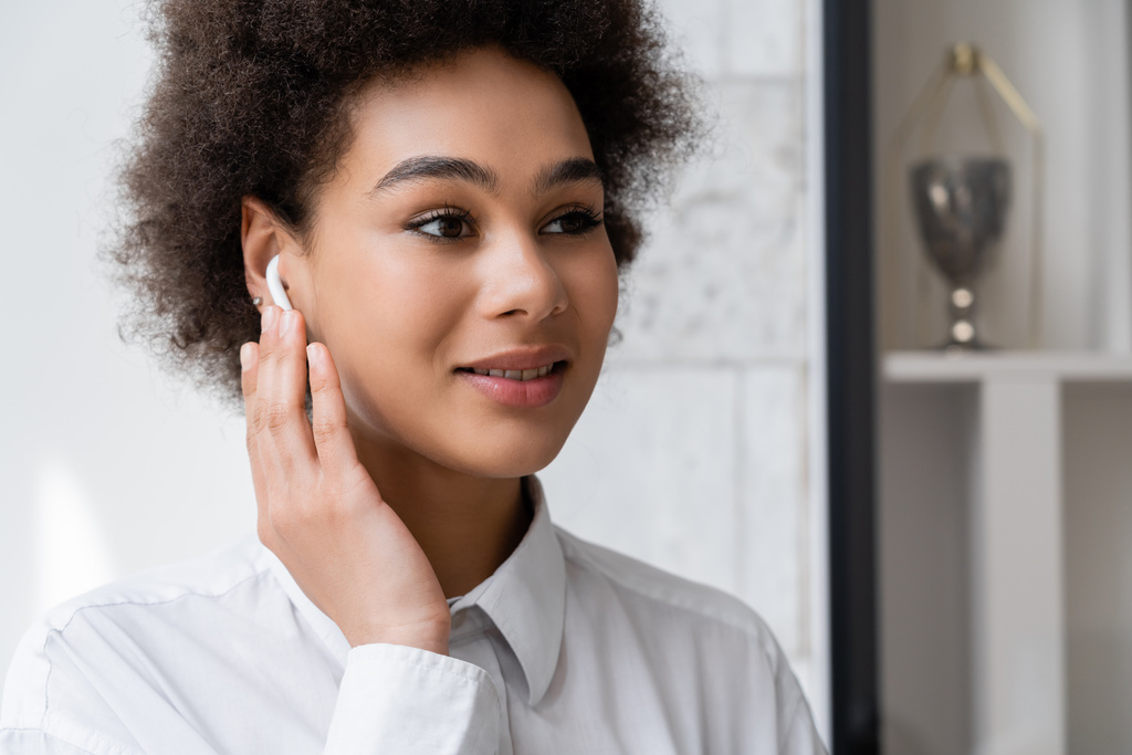 retrato de mulher americana africana feliz ouvindo música e ajustando fone de ouvido sem fio  - Foto, Imagem