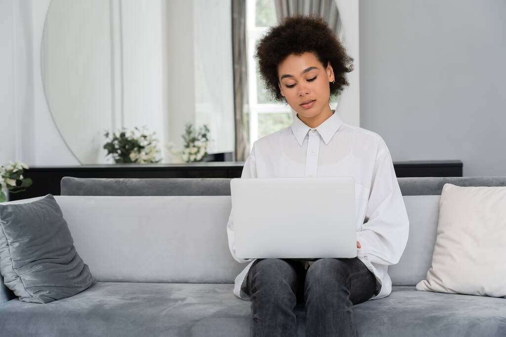 donna afro-americana che utilizza il computer portatile mentre lavora da casa in soggiorno moderno - Foto, immagini