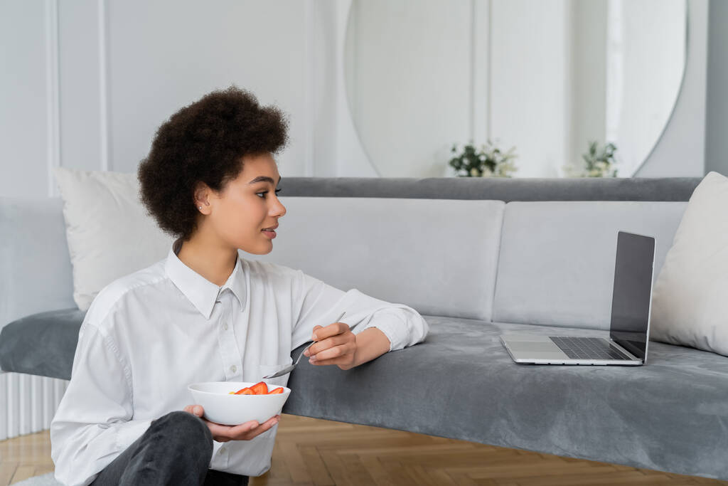вид збоку кучерявої афроамериканської жінки, що дивиться фільм під час сніданку у вітальні
  - Фото, зображення