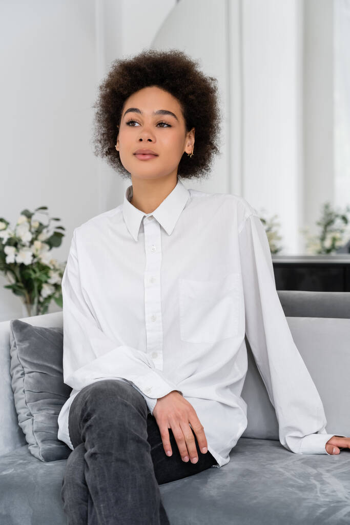 donna afroamericana pensierosa seduta sul divano grigio velluto - Foto, immagini