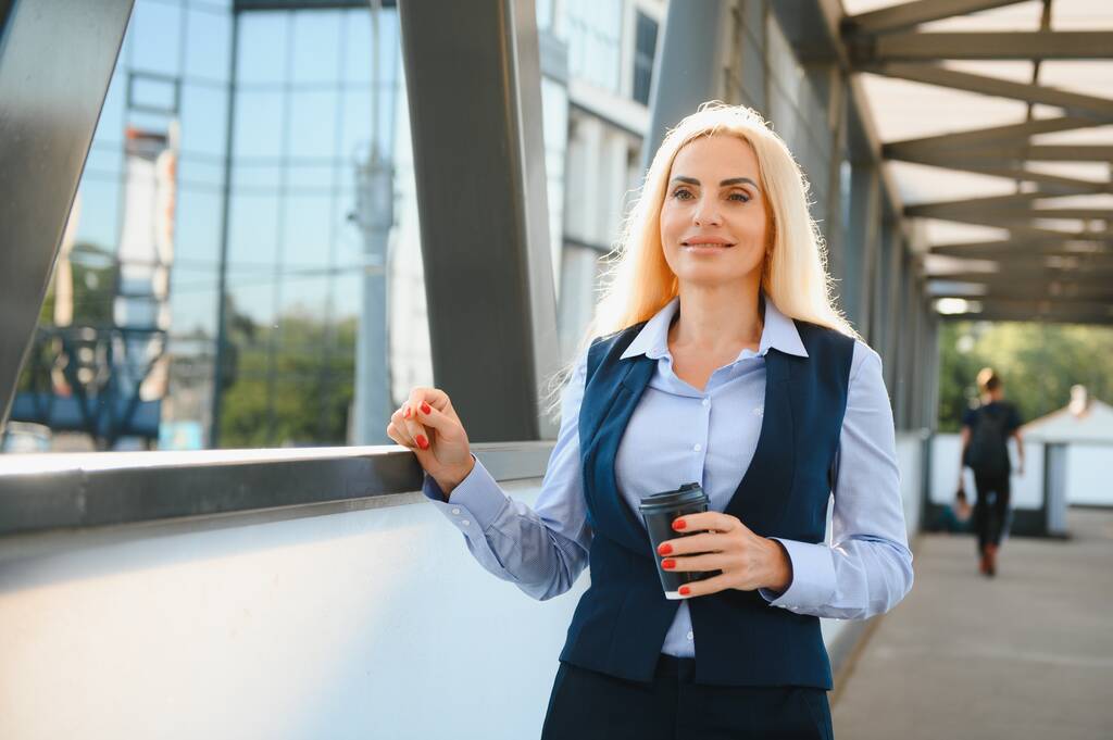Krásná žena jde do práce s kávou chůze v blízkosti kancelářské budovy. Portrét úspěšné obchodní žena drží pohár horkého nápoje - Fotografie, Obrázek