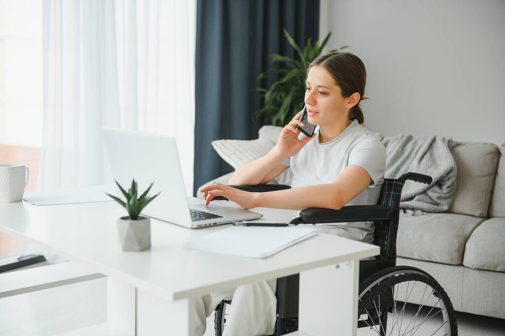 Programadora freelance sentada en silla de ruedas y usando computadoras mientras codifica el juego web en casa - Foto, imagen
