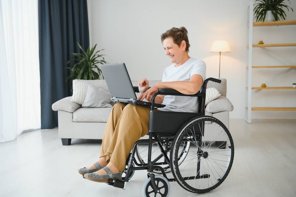 Позитивна літня жінка в інвалідному кріслі, що працює на ноутбуці, IT-фрілансер, онлайн
. - Фото, зображення
