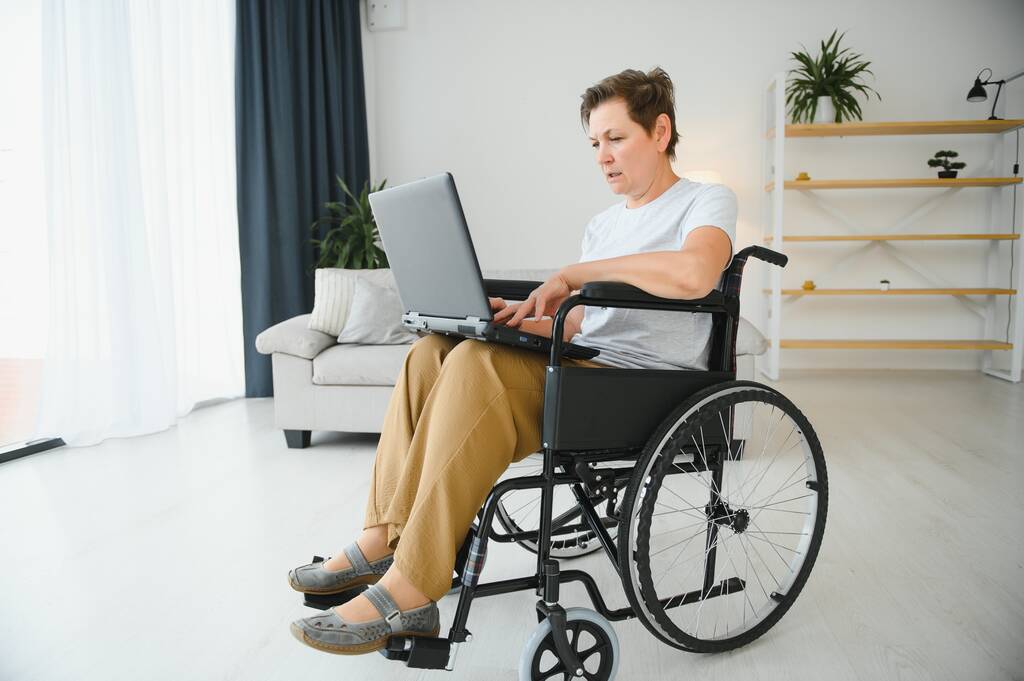 Mulher idosa positiva em cadeira de rodas trabalhando em laptop, freelancer de TI, online
. - Foto, Imagem