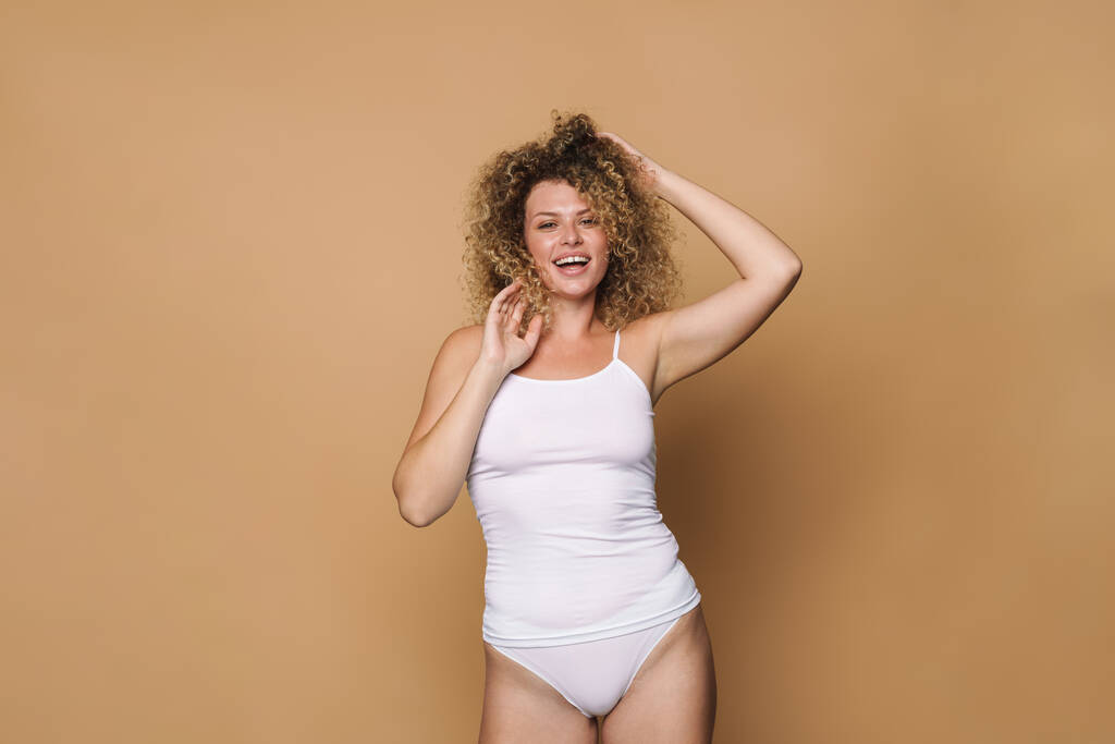 Mladá blondýna žena na sobě spodní prádlo se směje na kameru izolované přes béžové pozadí - Fotografie, Obrázek
