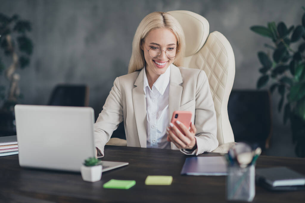 Портрет умной позитивной леди сидя кресло использовать телефон читать электронную почту современного офисного здания в помещении. - Фото, изображение