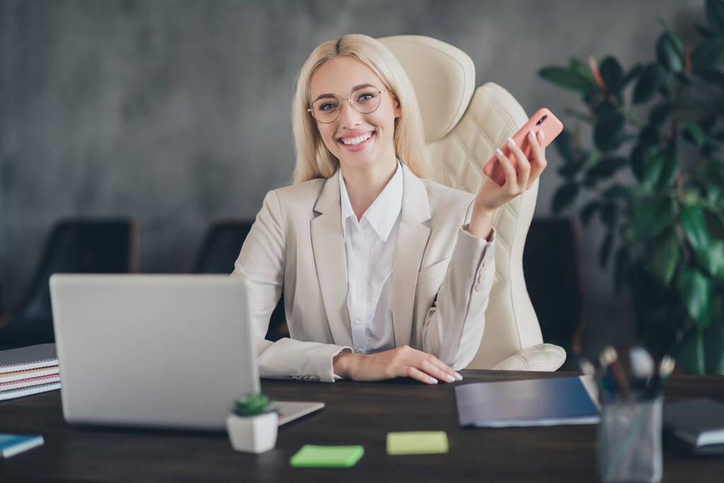 Foto de positivo encantador advogado senhora vestida jaqueta sorrindo comunicando dispositivo moderno dentro de casa oficina estação de trabalho. - Foto, Imagem