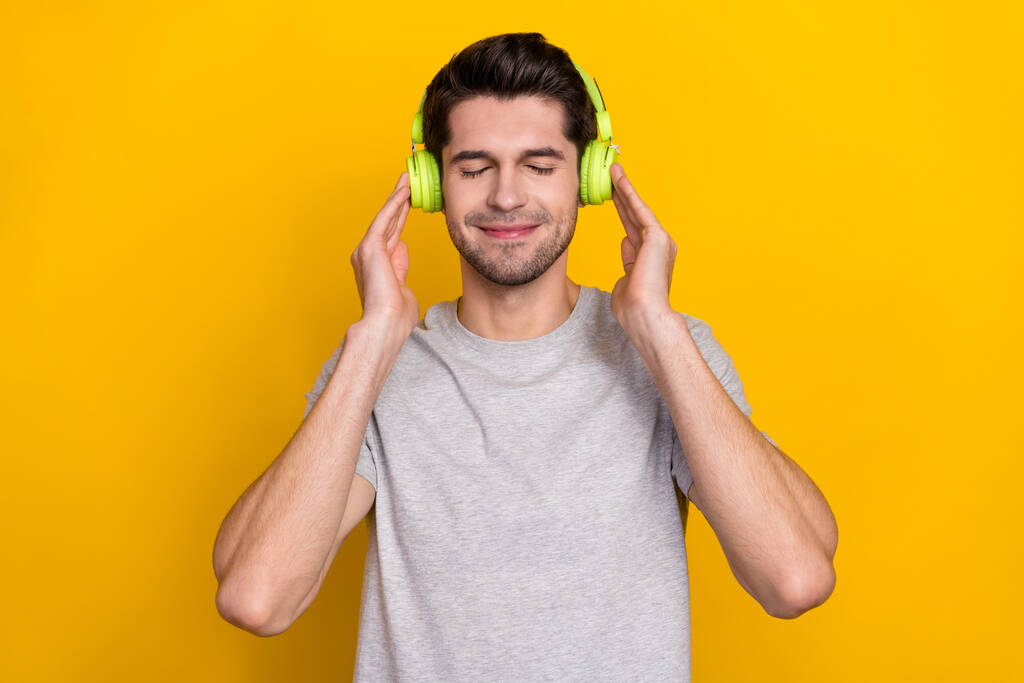 Foto de un agradable moreno millennial escuchar música usar auriculares camiseta gris aislado sobre fondo de color amarillo. - Foto, imagen