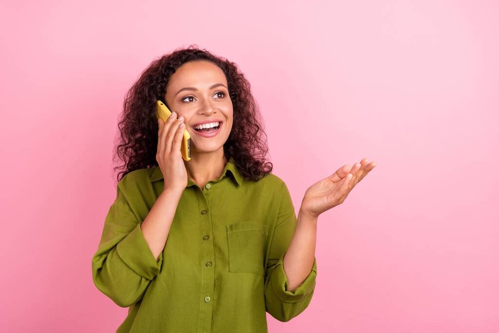 Photo de joyeux attrayant jeune afro américaine femme parler regarder vide espace téléphone isolé sur fond de couleur rose. - Photo, image